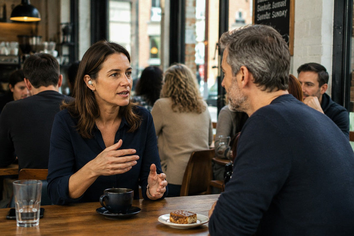 A man and woman having a conversation in a busy café, illustrating the challenge of hearing speech in background noise.